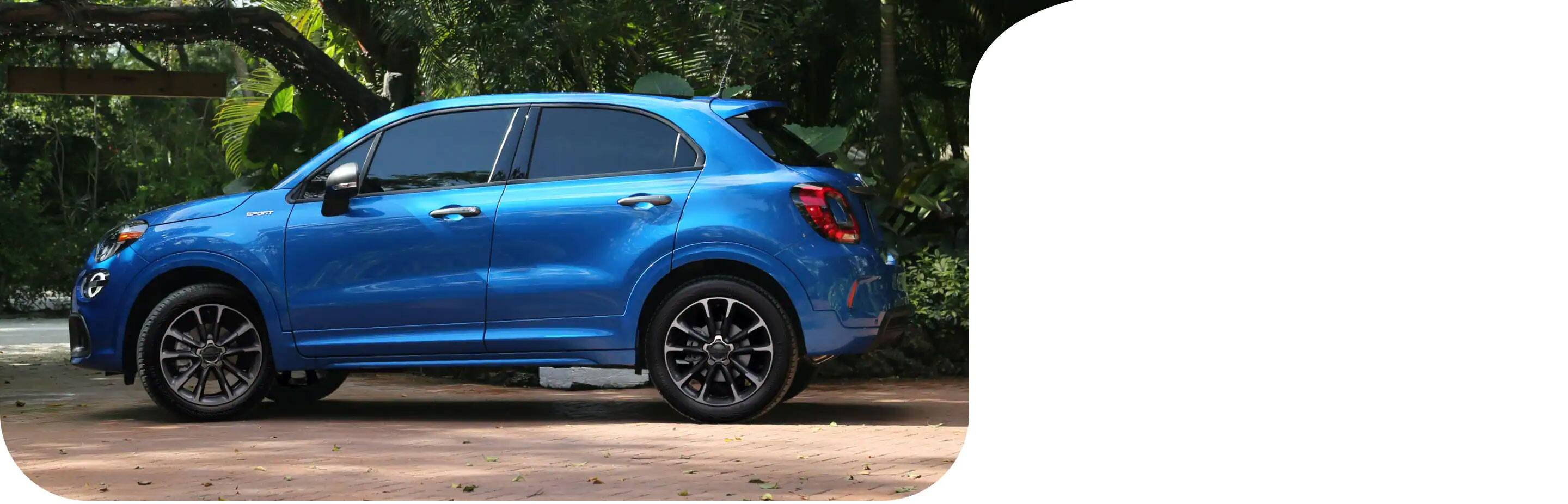 Vista de perfil de un Fiat 500X Sport 2021 azul estacionado en un barrio residencial al lado de un jardín exuberante.