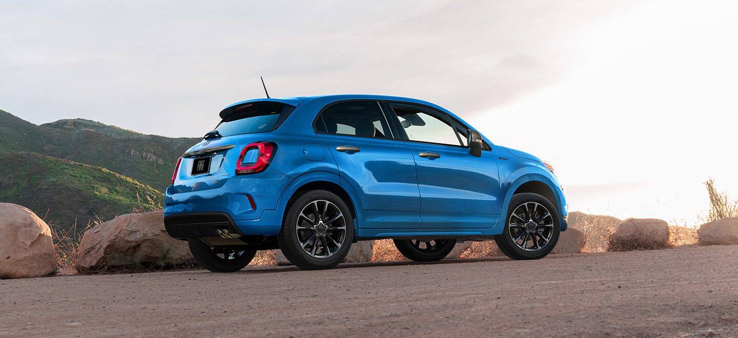 Display A three-quarter side view of a blue 2021 Fiat 500X Sport parked on a plateau with green hills in the background.