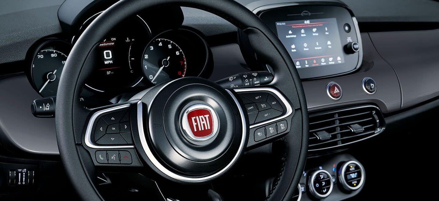 Vista El interior del Fiat 500X Trekking 2021, con el foco puesto en el volante, la pantalla digital con información para el conductor en el panel de instrumentos y la pantalla táctil Uconnect.