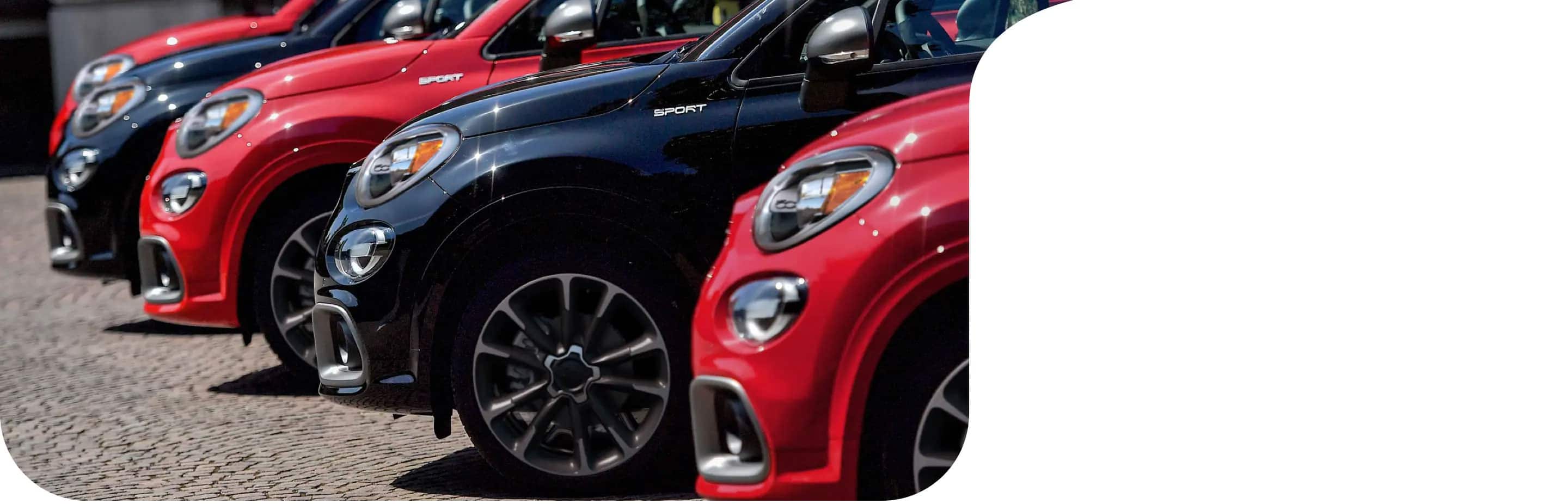 A close-up of the driver-side front end of five 2022 Fiat 500X Sport models parked side-by-side in alternating colors: red and black.