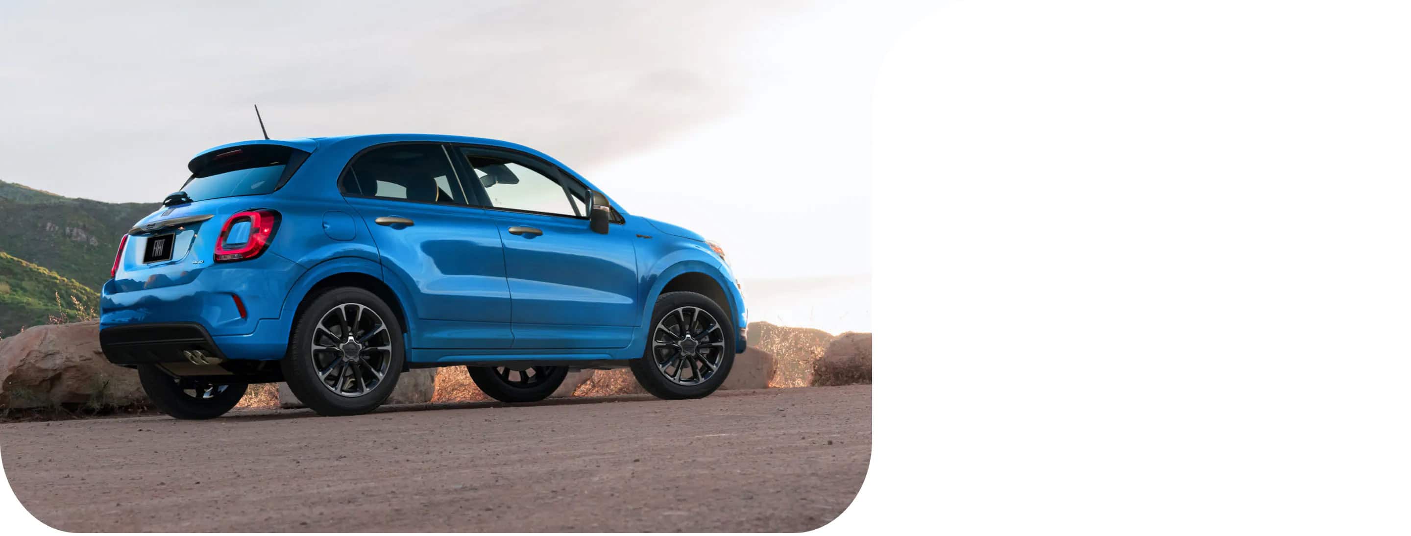 A three-quarter rear profile view of a blue 2022 Fiat 500X Sport parked on the shoulder of a highway beside a mountain.