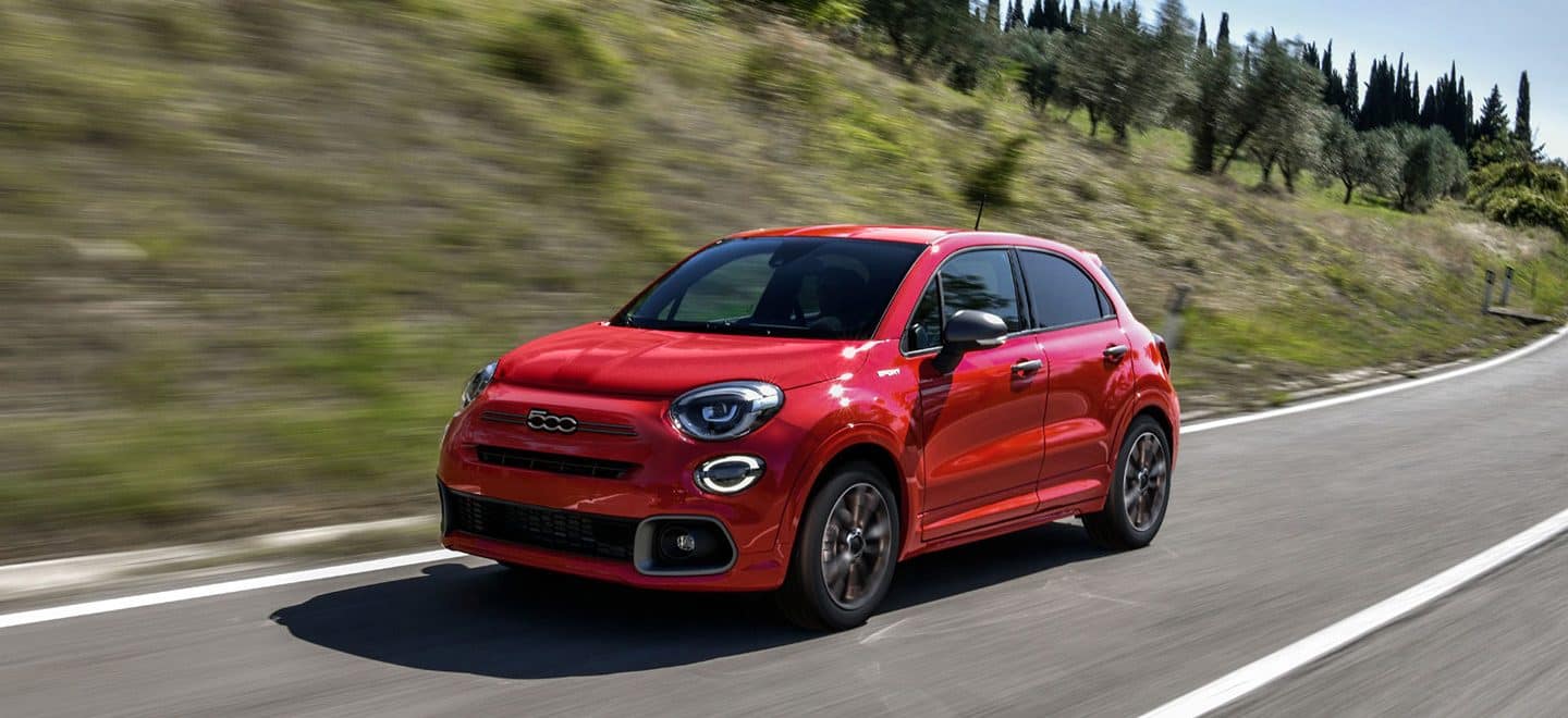 Display An angled front view of a red 2023 Fiat 500X Sport driving on a highway. 