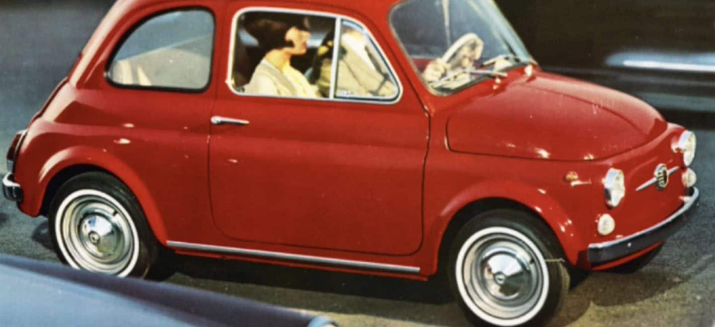 Display A vintage photo of a classic Fiat 500 being driven on the street with a couple in the front street.