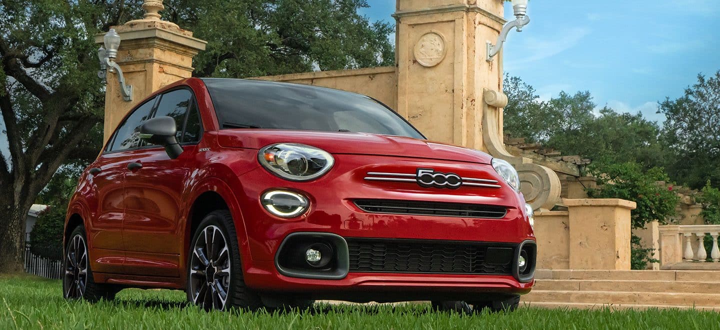 Display A three-quarter front view of a red 2022 Fiat 500X Sport parked beside sculptured columns.