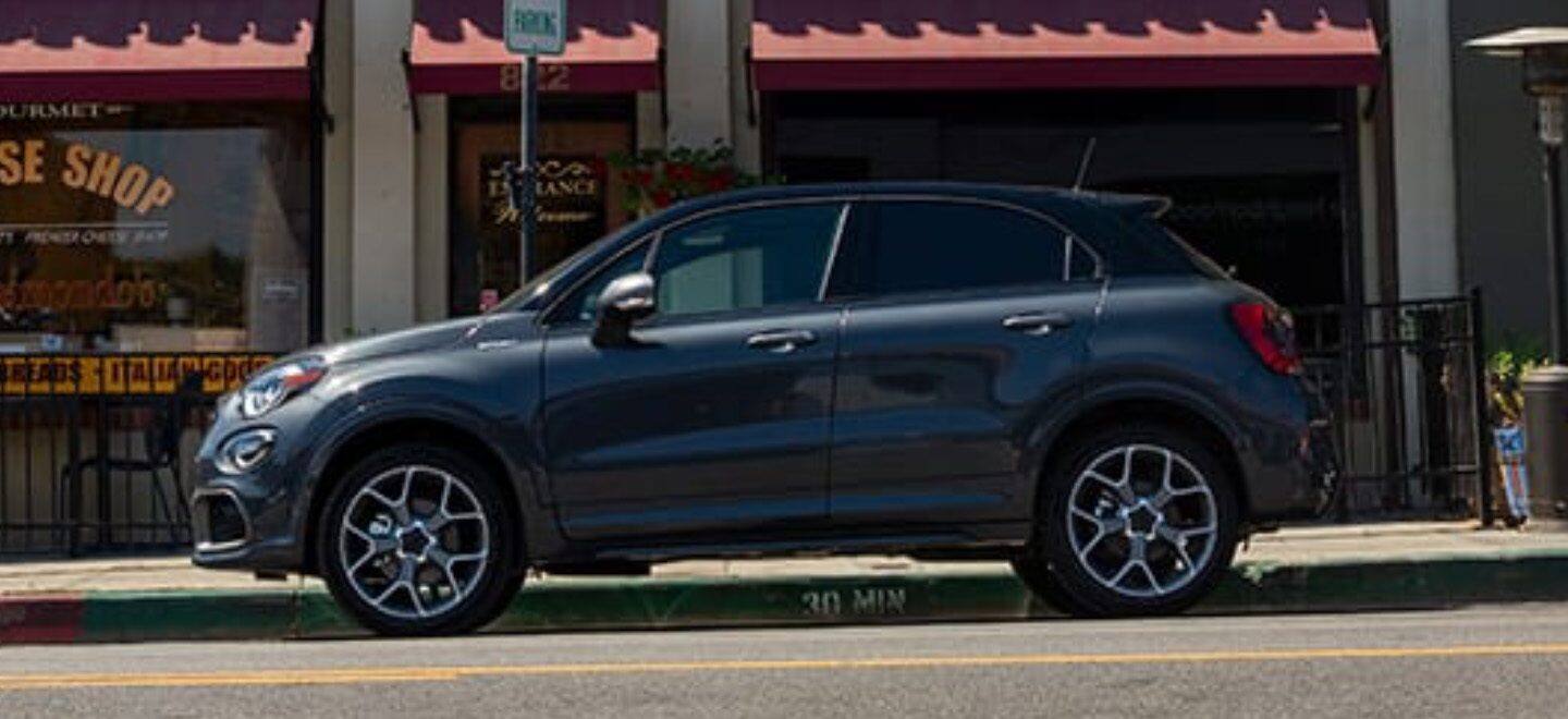 Display A profile view of a 2021 Fiat 500X Sport parked in front of a quaint cheese shop.