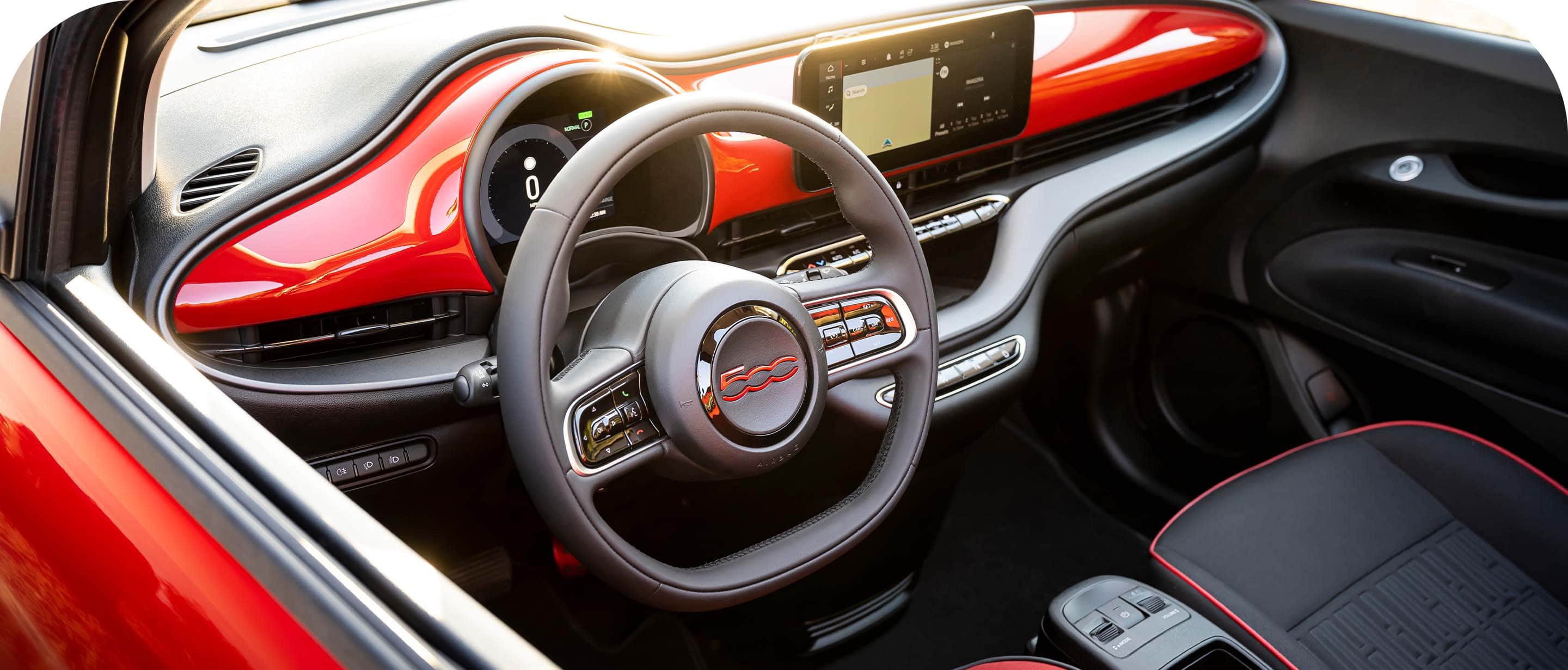 The interior of the 2024 Fiat 500e Red, focusing on the steering wheel, Uconnect touchscreen and dash.
