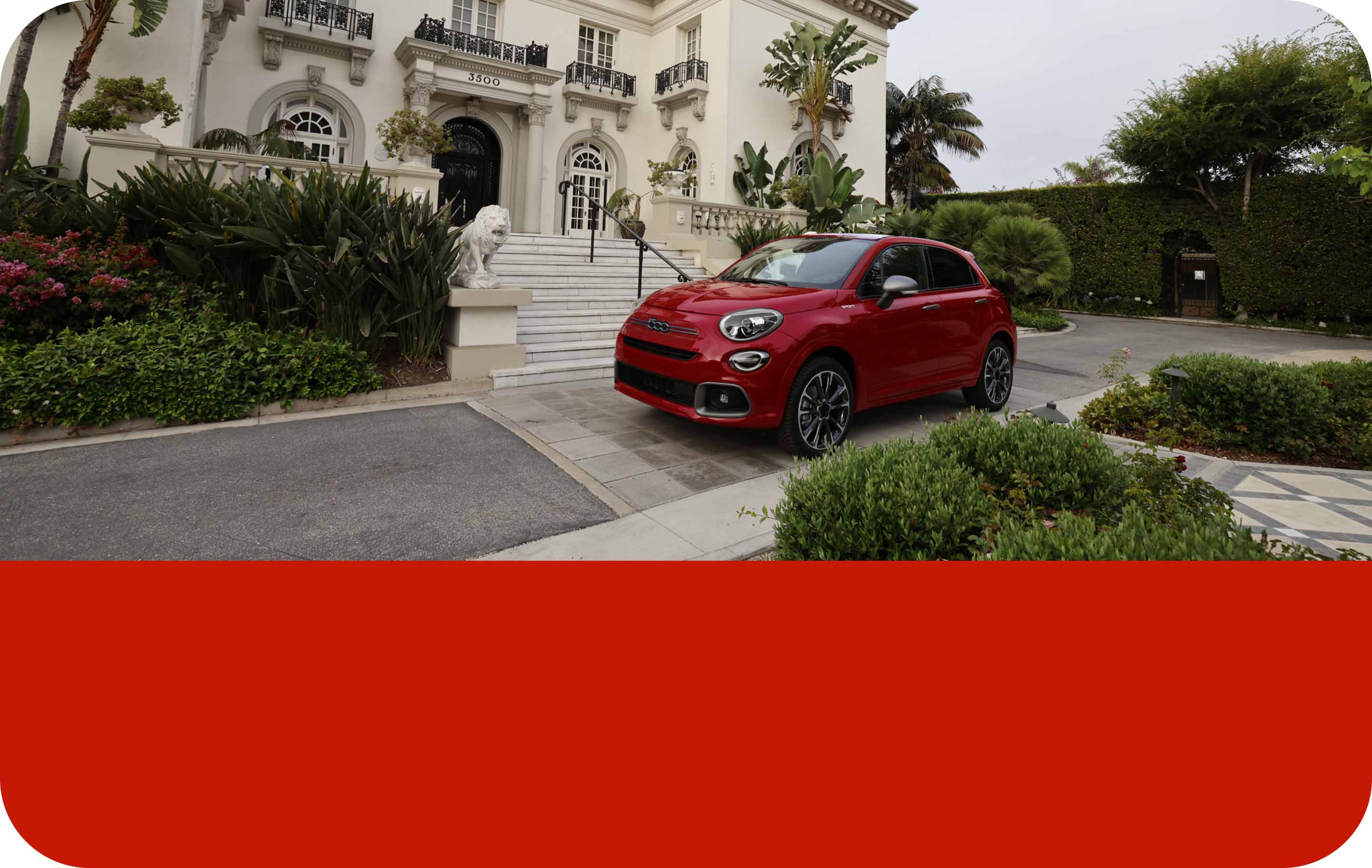 An angled front driver-side profile of a red 2023 Fiat 500X Sport, parked in the driveway of an affluent home. 