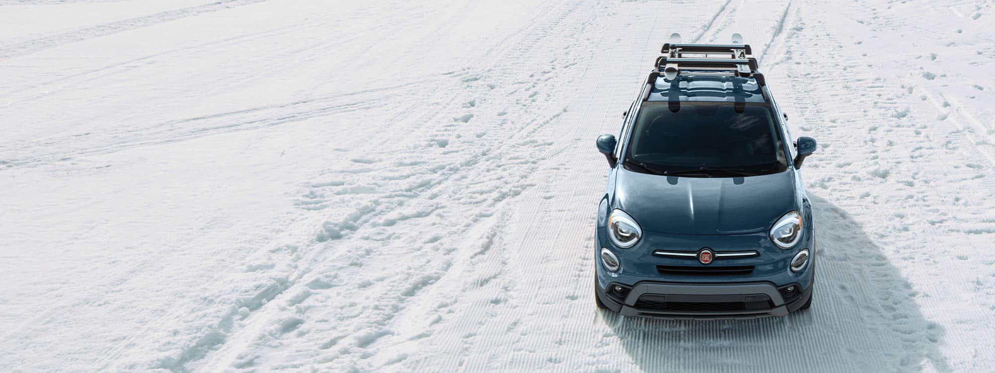 A raised, head-on view of a 2021 Fiat 500X Trekking with aftermarket equipment, being driven through snow.