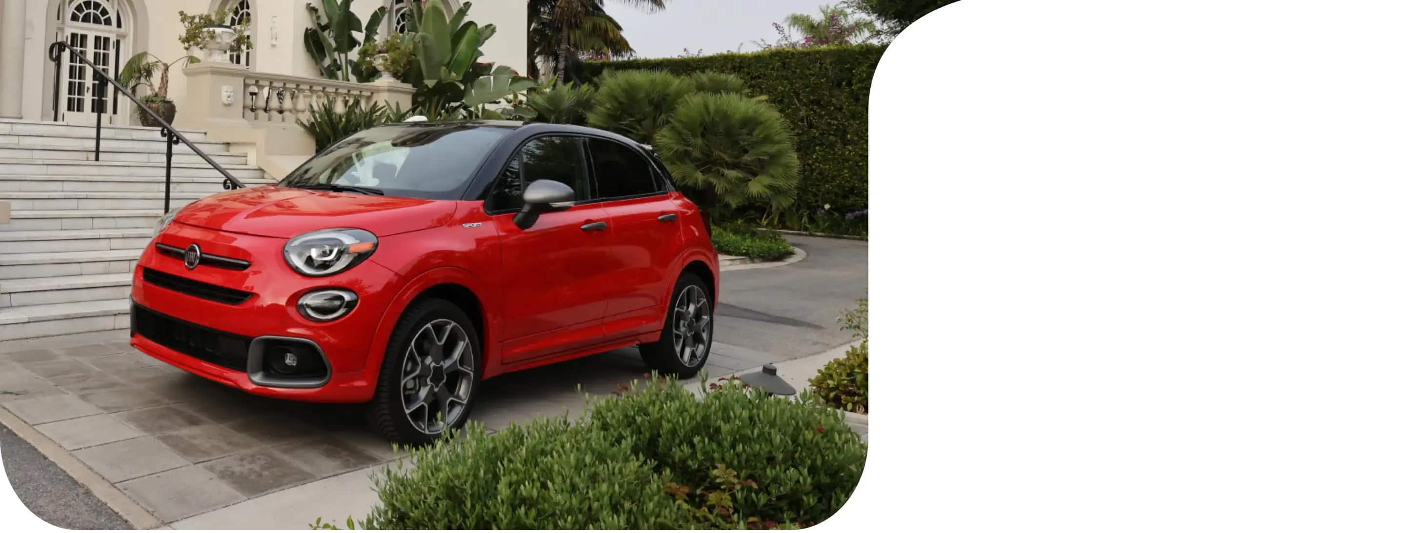 A three-quarter front view of a red 2021 Fiat 500X Sport parked next to an opulent home.