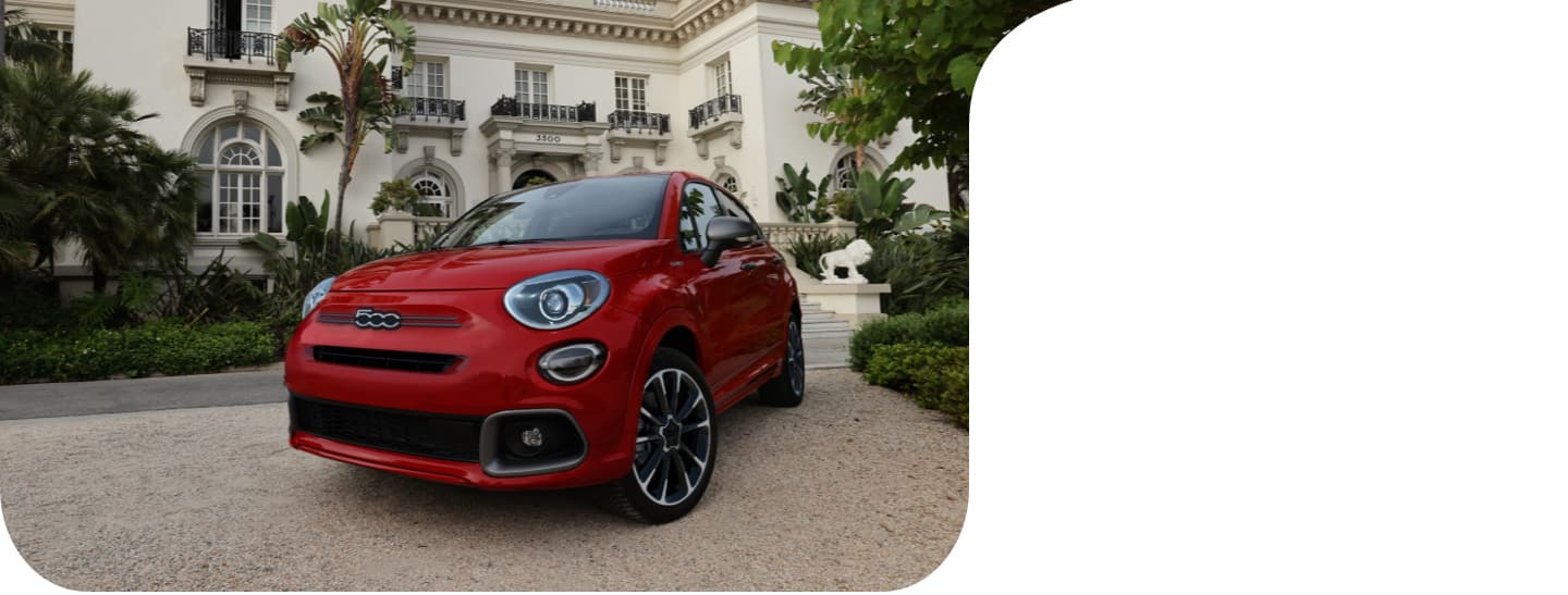 A profile view of a blue 2021 Fiat 500X Sport parked in a residential neighborhood beside a lush garden. 