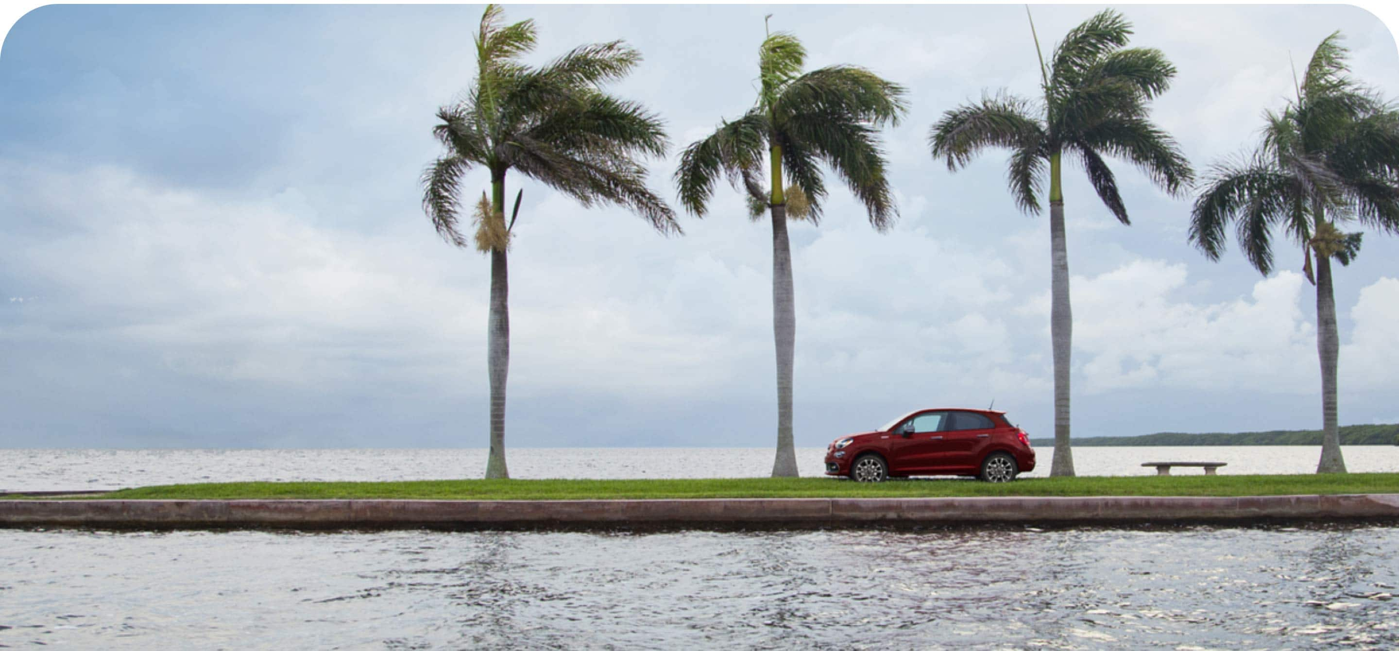 A profile view of the 2022 Fiat 500X Sport parked next to the beach with four palm trees towering overhead.