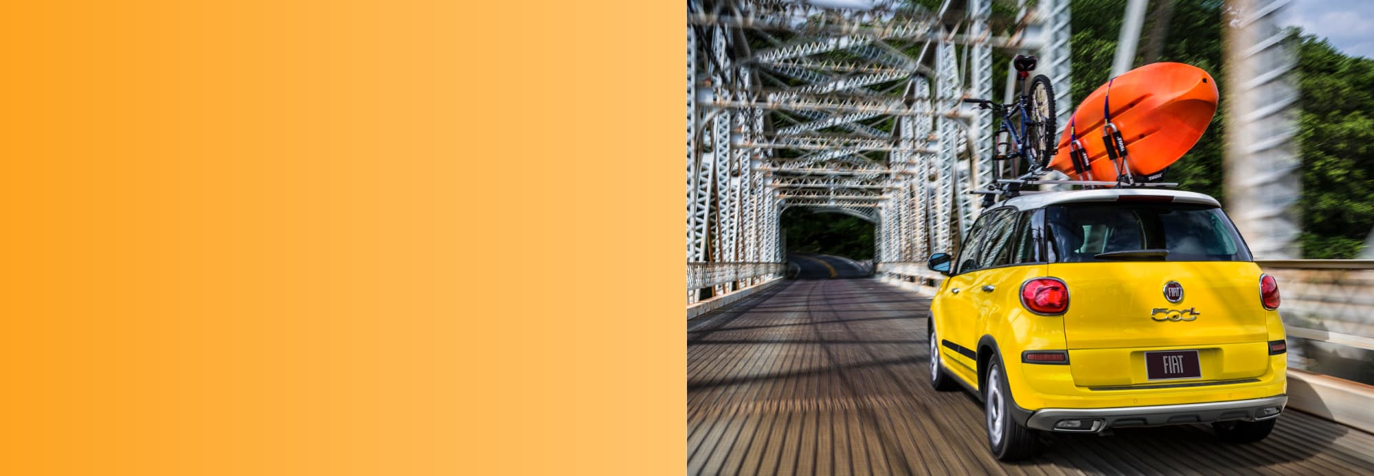 A rear view of a yellow 2020 Fiat 500L Trekking being driven across a bridge.