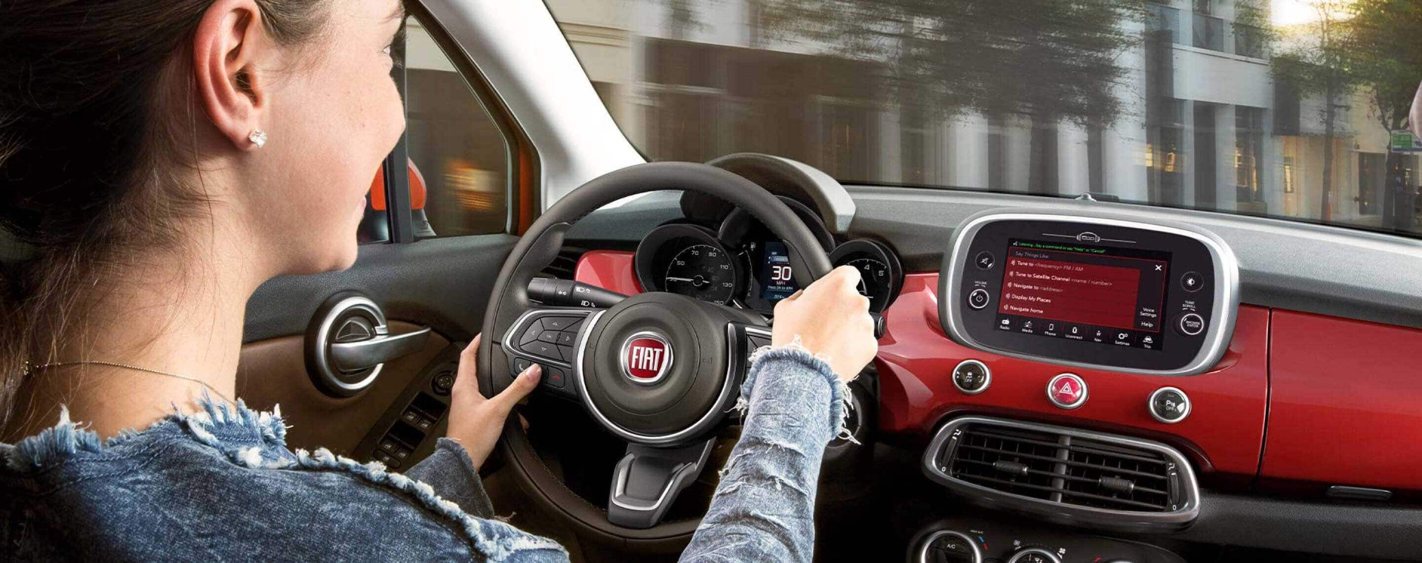 The driver of a 2021 Fiat 500X Trekking Plus watching the road while pressing one of the buttons on the steering wheel-mounted controls.
