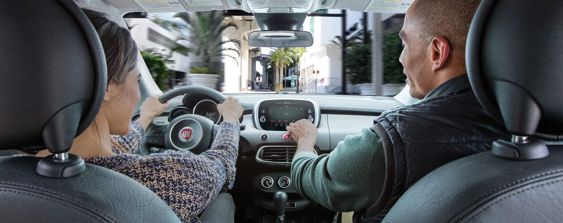 The interior of a 2021 Fiat 500X Trekking Plus with a man in the front passenger seat using the Uconnect touchscreen.