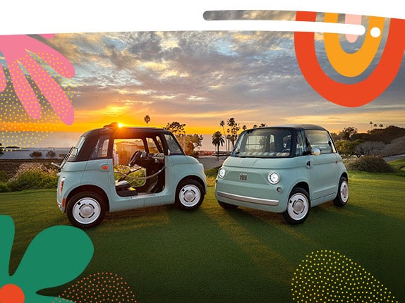 Two mint green preproduction model Fiat Topolino models parked opposite of each other on a golf course at sunset. On the left, a Topolino Dolce Vita with door ropes and a rolled-up soft top, and on the right a Topolino.