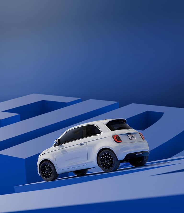 A driver-side rear angle of a white 2025 Fiat 500e Icona, behind and below it a backdrop of geometric shapes all in shades of blue.