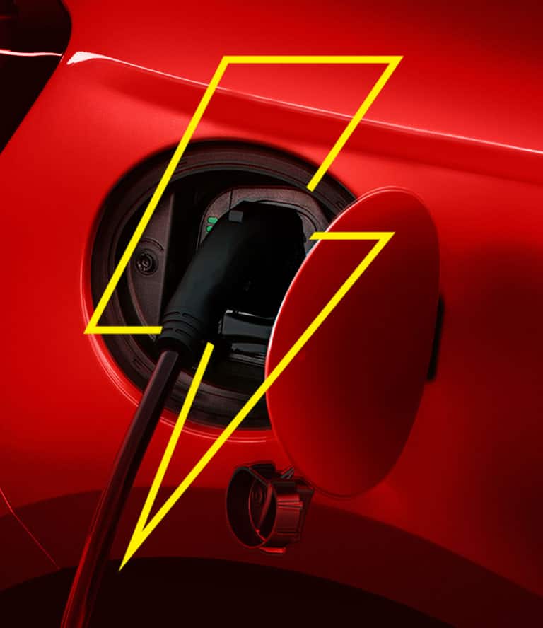 A hand plugging a charging cord into the charging port on a 2025 Fiat 500e Icona.