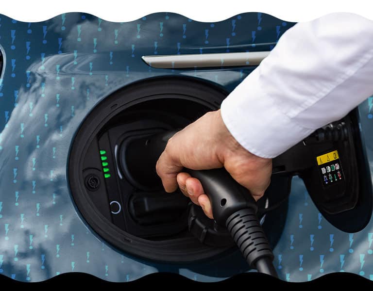 A hand plugging a charging cord into the charging port on a 2025 Fiat 500e Icona.