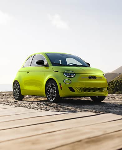 A lime green 2026 Fiat 500e Pop parked on a beach beside a boardwalk.