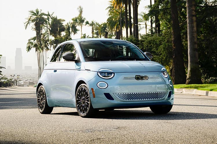 A light blue 2026 Fiat 500e Icona parked on a street with palm trees in the background.