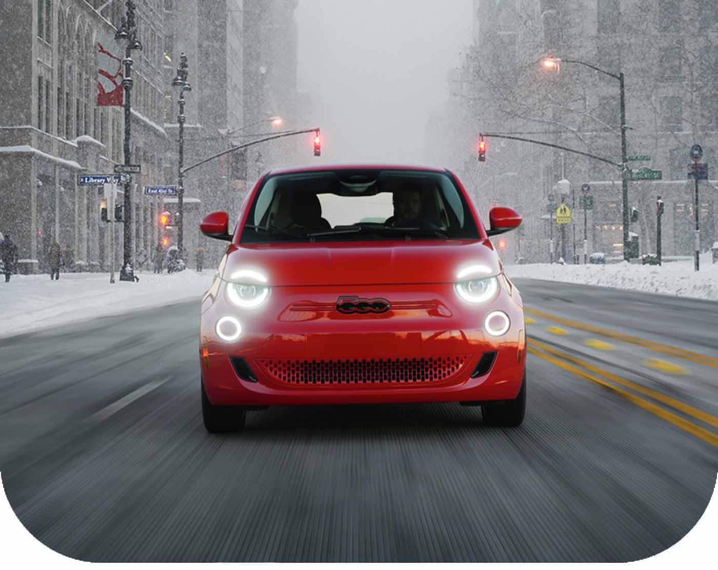 Ángulo frontal de un Fiat 500e 2024 circulando por la calle de una ciudad en invierno durante una tormenta de nieve.