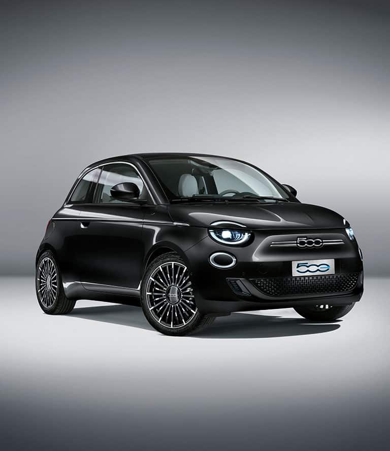 An angled passenger-side front profile of a black 2024 European model Fiat 500e La Prima in a studio.