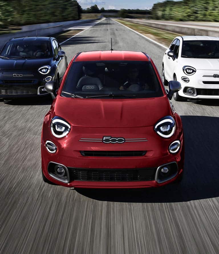 A head-on angle of three 2023 Fiat 500X Sport models being driven on a track. From left to right: One blue, one red and one white.
