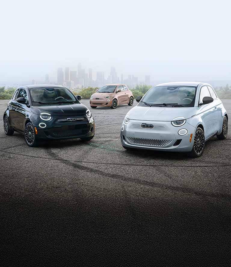 Tres modelos Fiat 500e models estacionados en un semicírculo. De izquierda a derecha: nn Fiat 500e Icona 2025 negro, un Fiat 500e Icona 2025 oro rosa y un Fiat 500e 2025 azul.