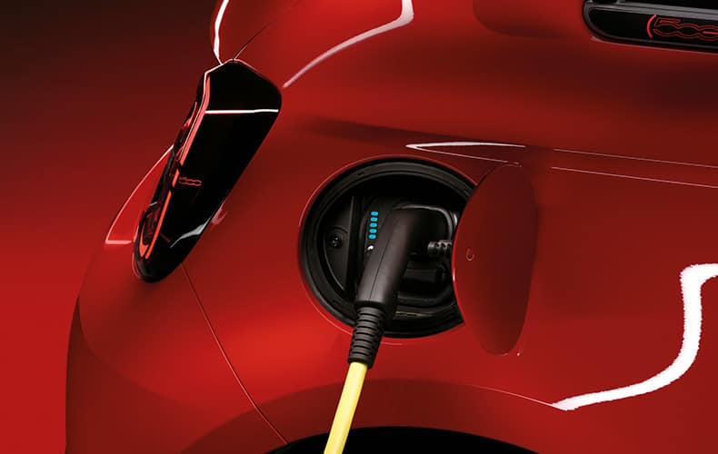 The charging port on a red 2025 Fiat 500e Red, with a charging cord plugged in to it.