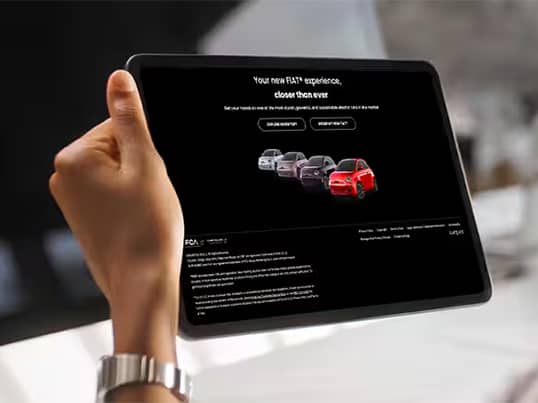 A close-up shot of a hand holding a tablet on which someone is shopping for a Fiat vehicle online.