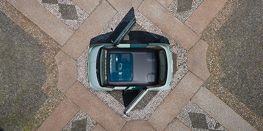 An overhead angle of a mint green European model Fiat Topolino with a fixed glass roof and its solid doors open, parked in an elegant courtyard.