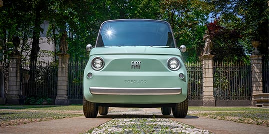 A head-on angle of a mint green European model Fiat Topolino parked at the entrance of a gated estate.