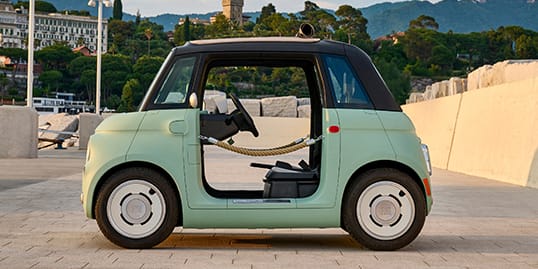A driver-side profile of a mint green European model Fiat Topolino Dolce Vita with door ropes, parked on a brick driveway.