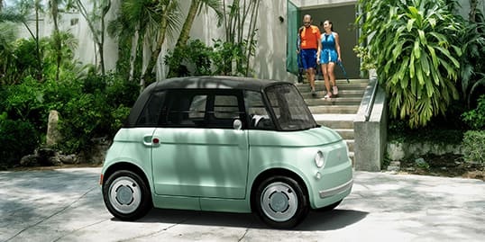 A head-on angle of a mint green European model Fiat Topolino parked at the entrance of a gated estate.