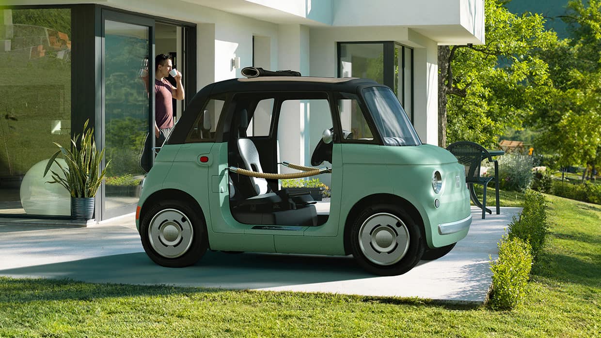 A mint green European model Fiat Topolino Dolce Vita with door ropes, parked in the driveway of a contemporary home.