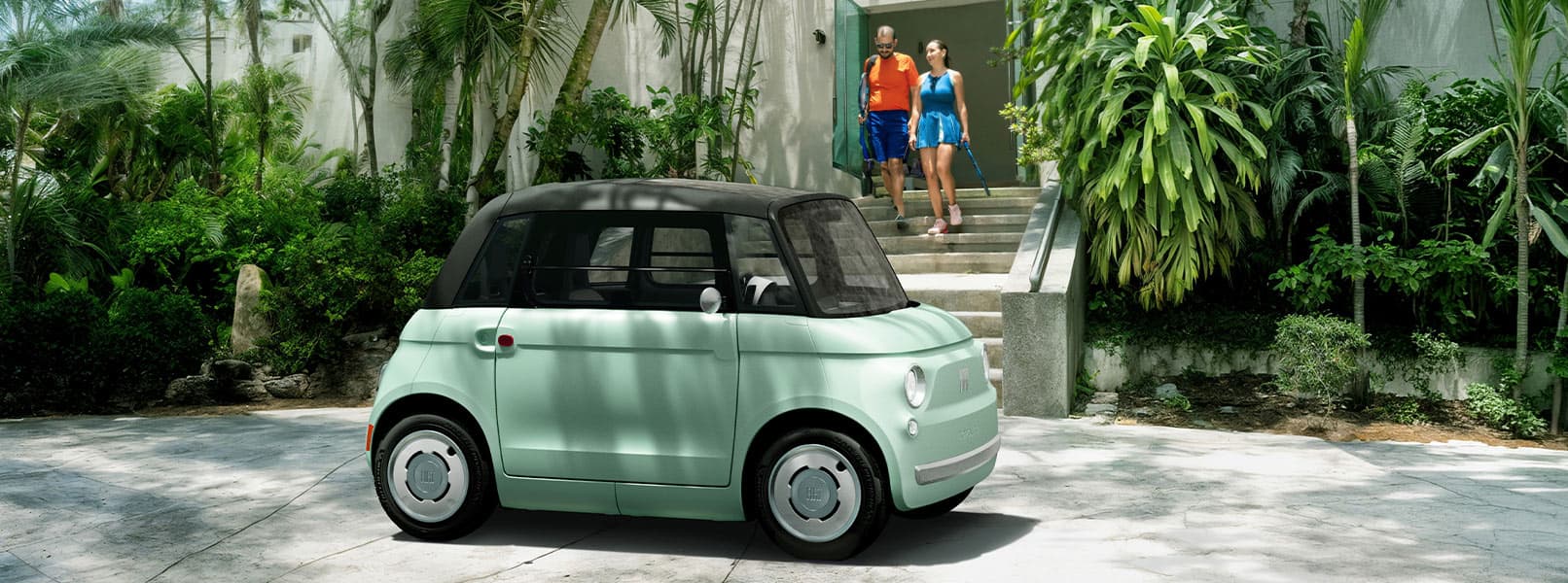 A mint green preproduction model Fiat Topolino parked in front of a tennis club, with a couple exiting the club.